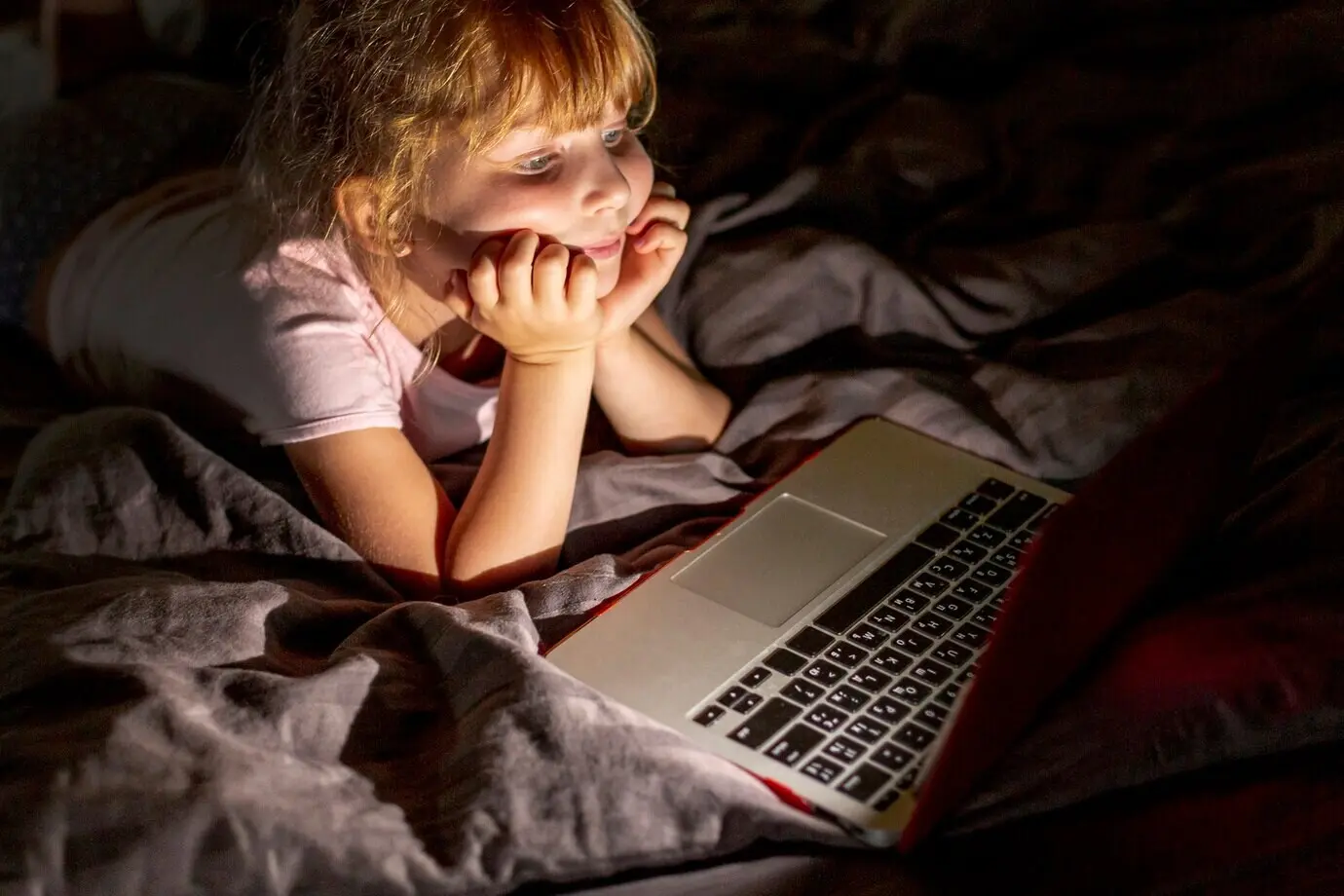 Side view of a smiling girl in bed with a laptop.