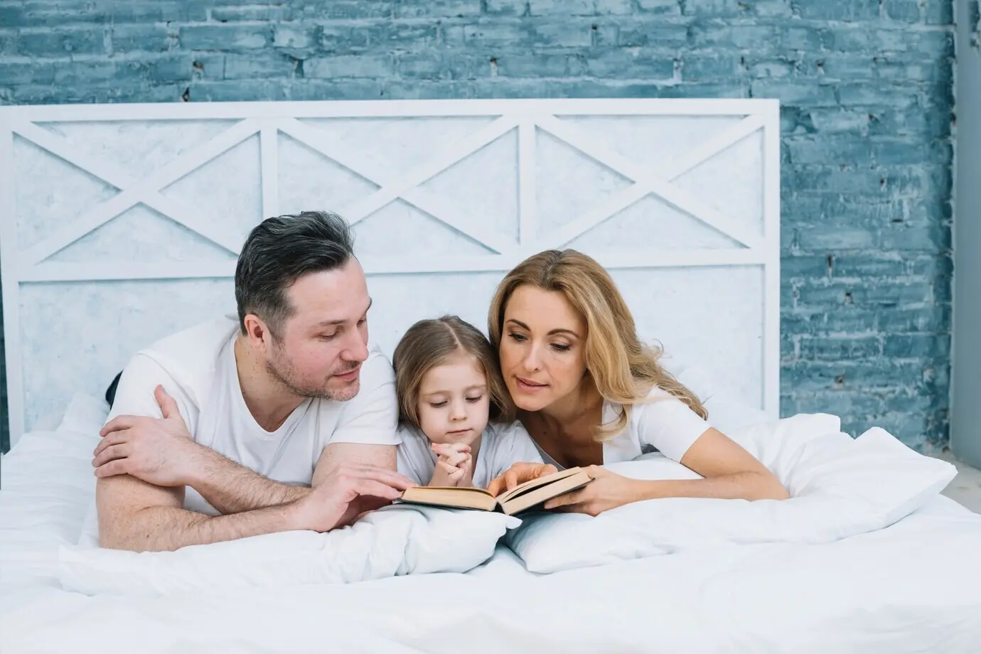 A family reads a book on a bed.